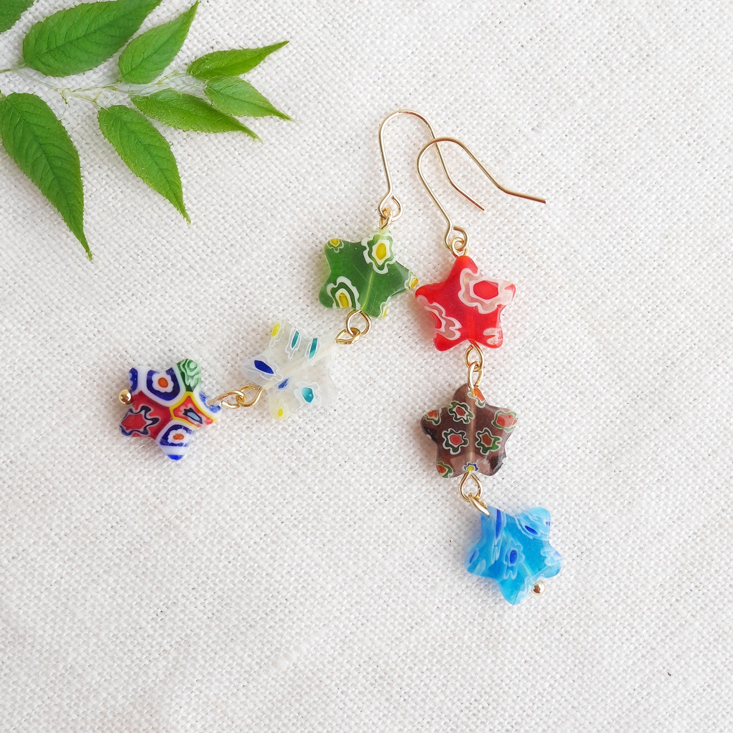 Colorful star dangle earrings with three millefiori star shape glass beads in each earring, on a white cloth.