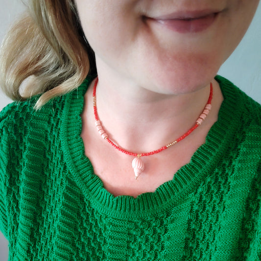 Woman wearing a beaded red conch shell necklace.