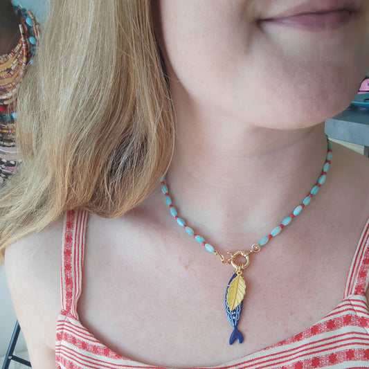 Woman wearing turquoise red beaded necklace with fish and leaf charm.