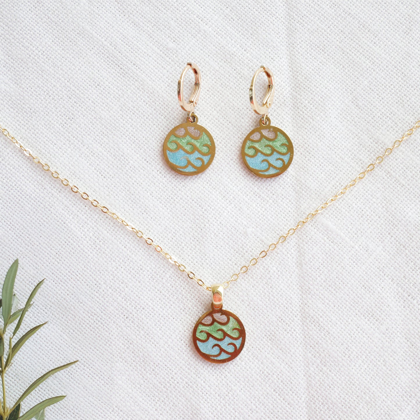 Wave gold disc charm necklace with a pair of earrings on a white cloth.