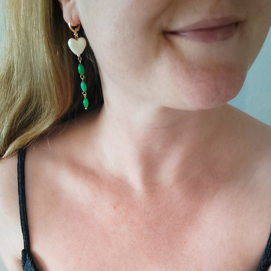 Woman wearing heart-shaped earrings with white porcelain heart and green shell beads.