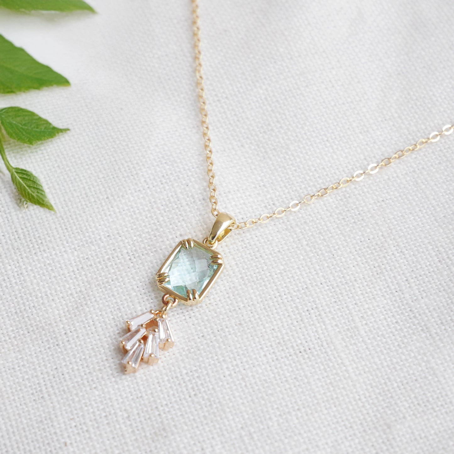 Art deco style lake blue glass gold necklace, on a white cloth.