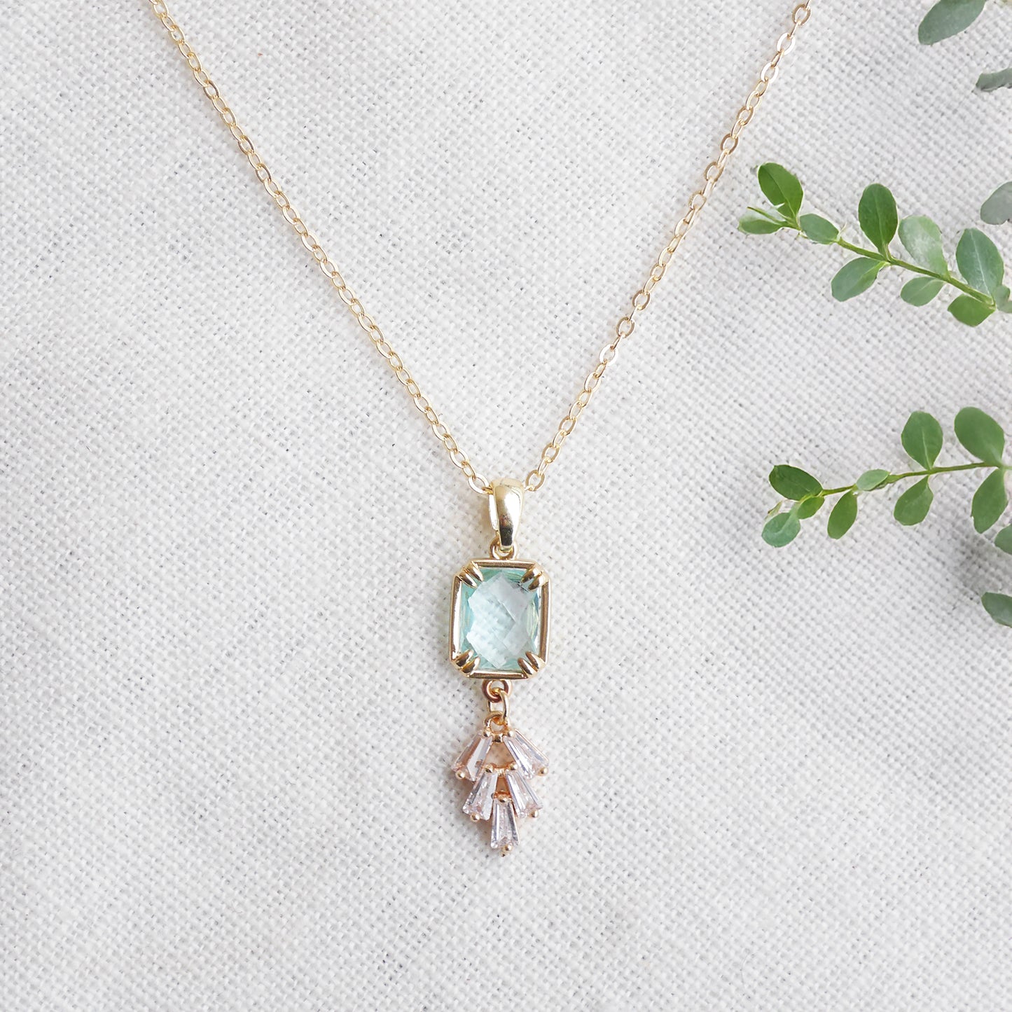 Art deco style lake blue glass gold necklace, on a white cloth.