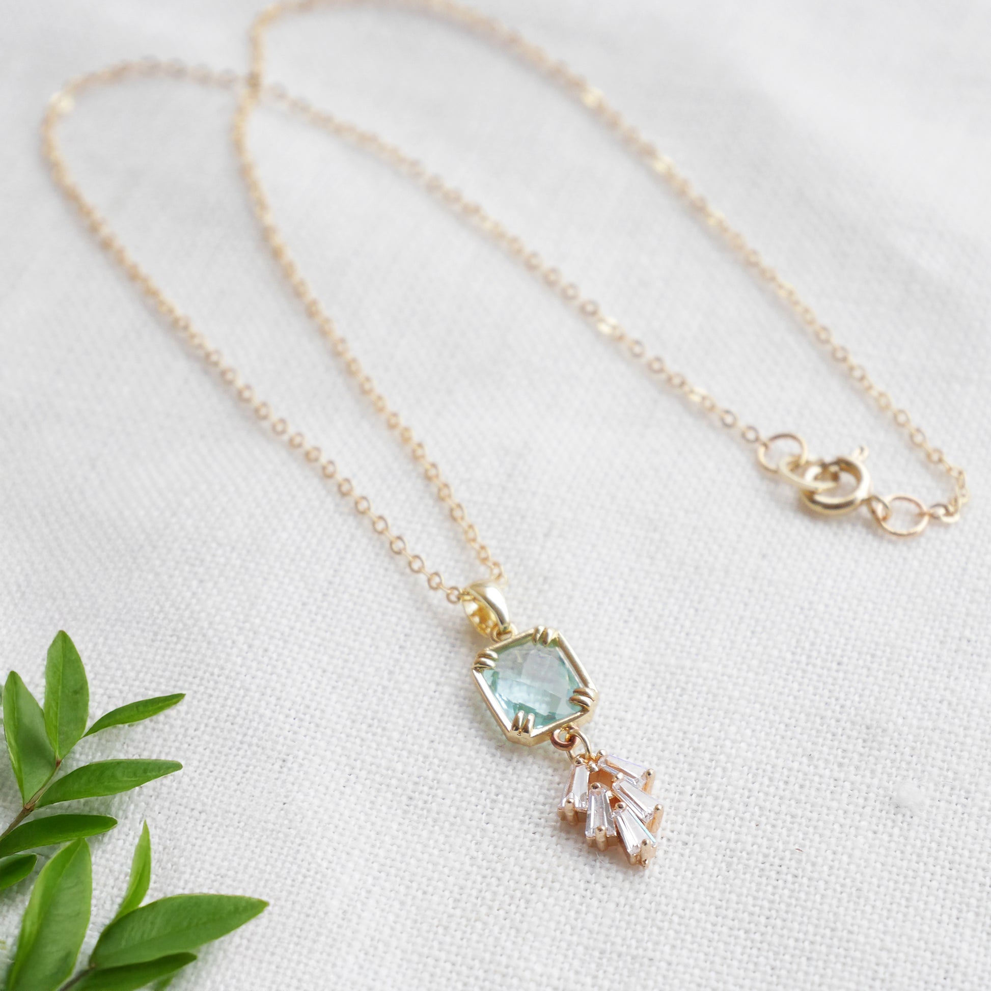 Art deco style lake blue glass gold necklace, on a white cloth.