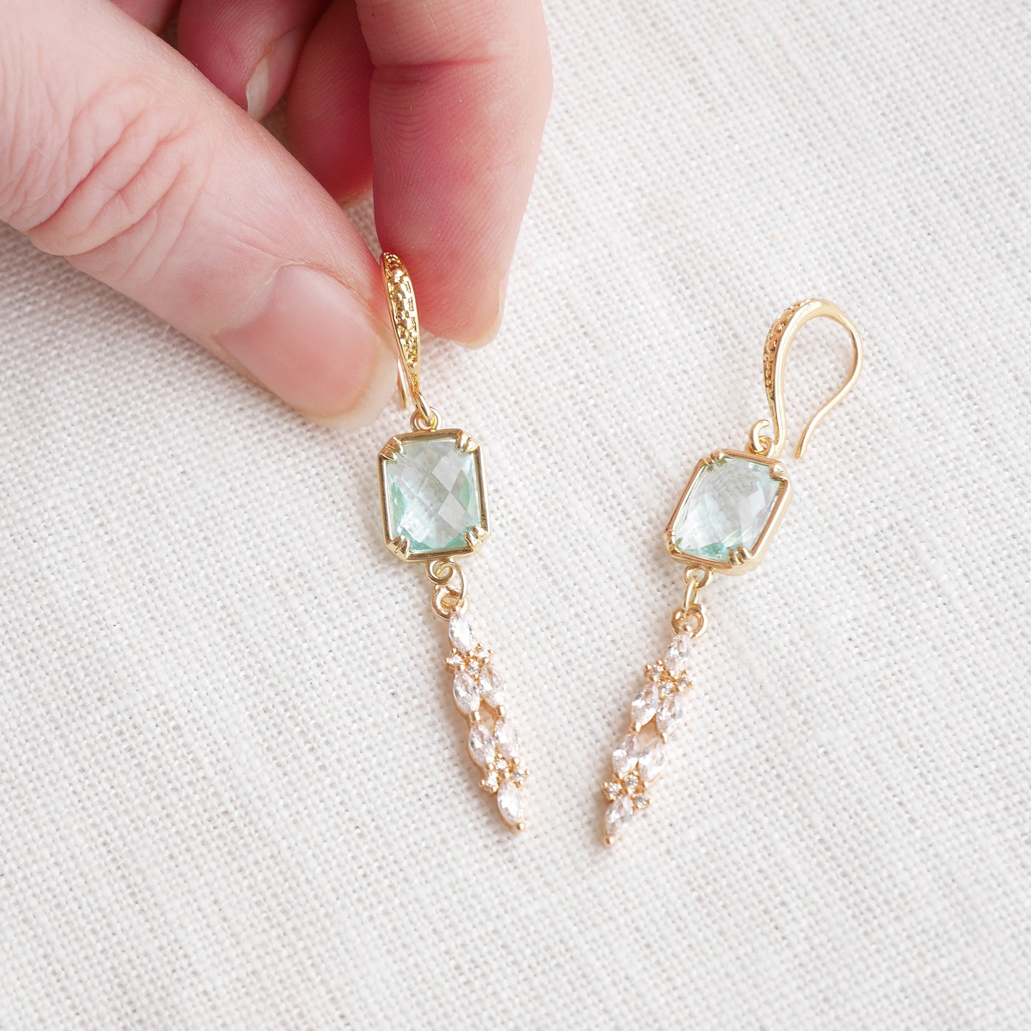 Long light blue glass bridal dangle earrings on a white cloth.