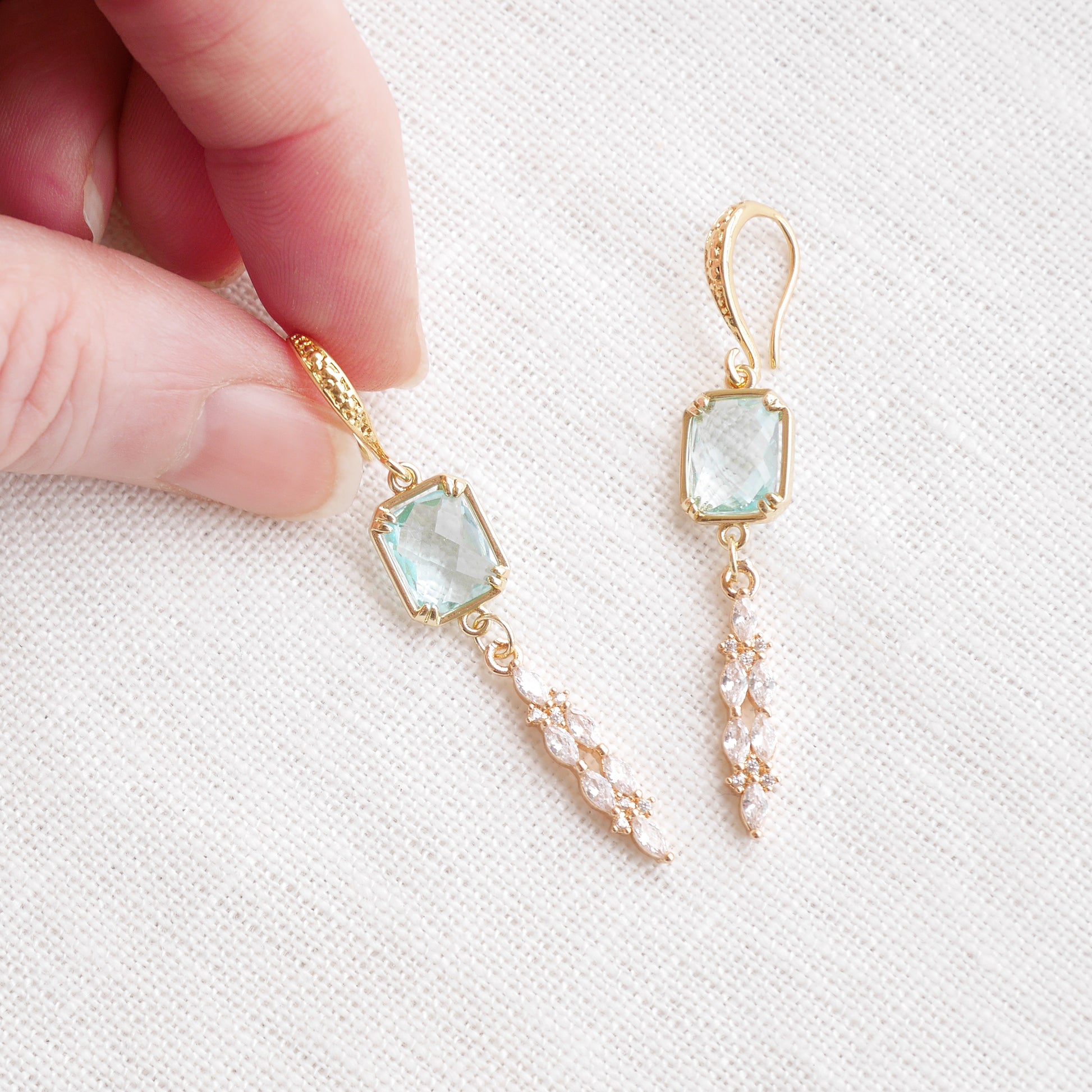 Long light blue glass bridal dangle earrings on a white cloth.