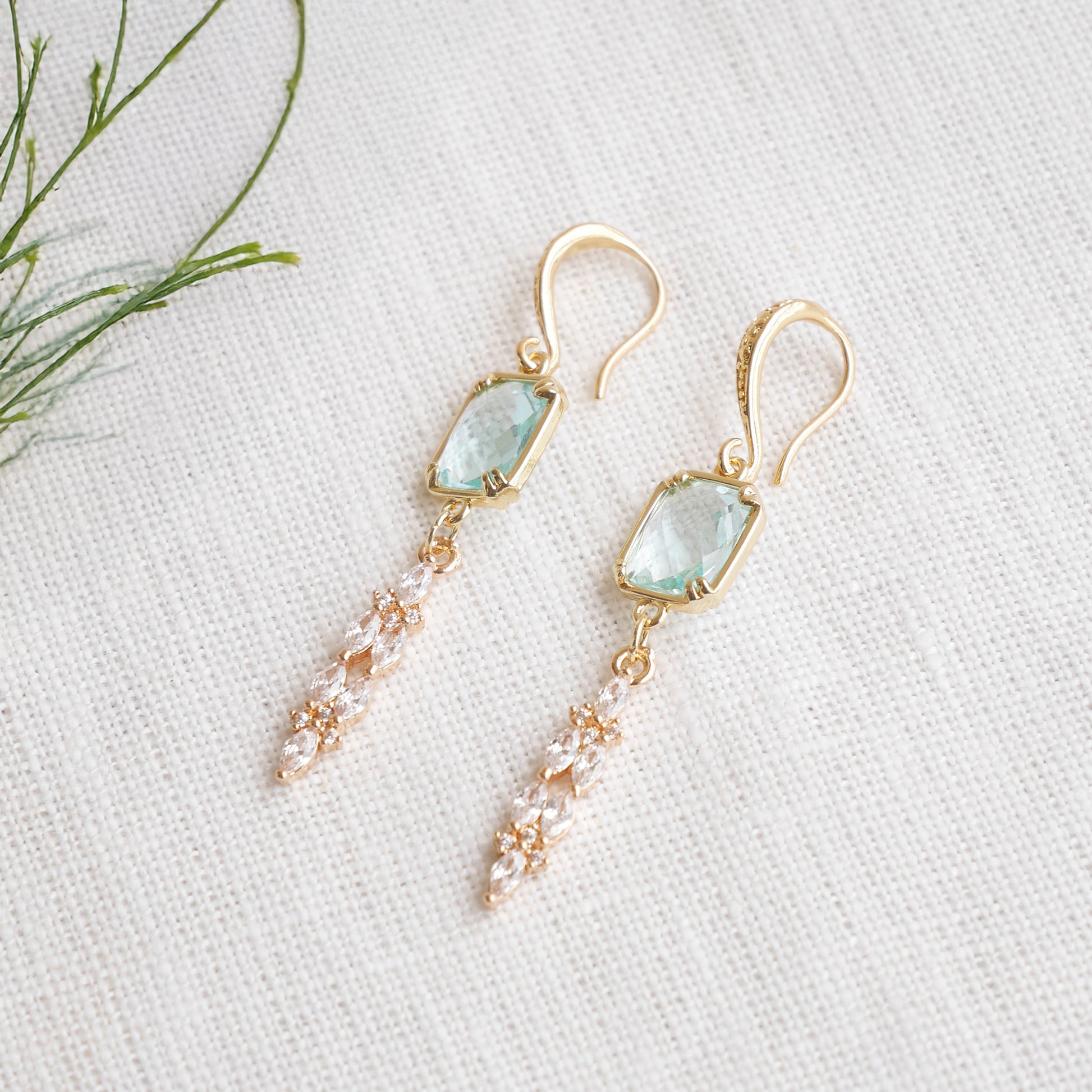 Long light blue glass bridal dangle earrings on a white cloth.