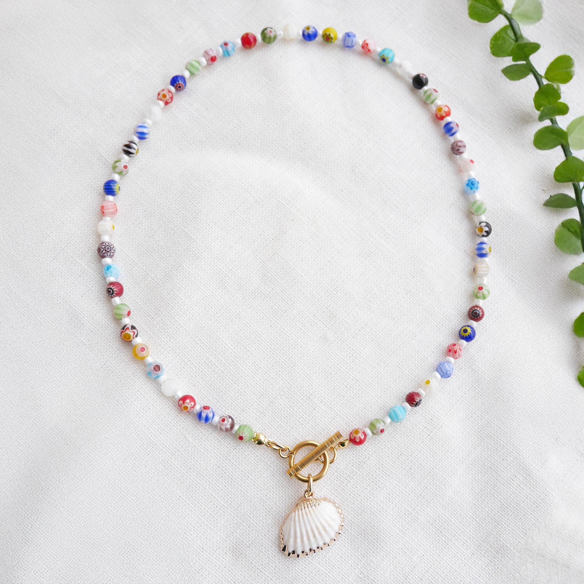 Colorful millefiori necklace with a seashell charm on a white cloth