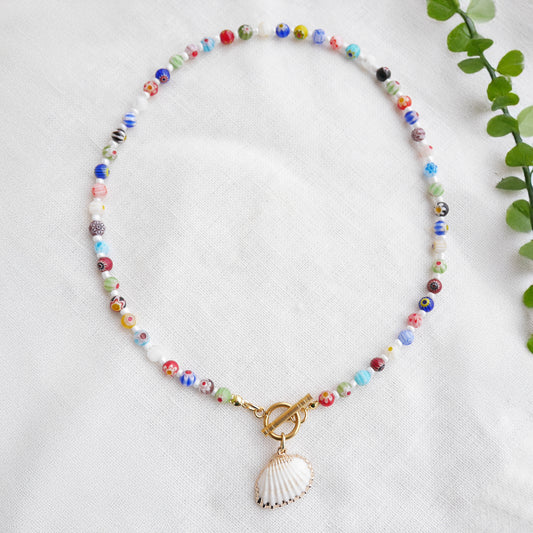 Colorful millefiori necklace with a seashell charm on a white cloth