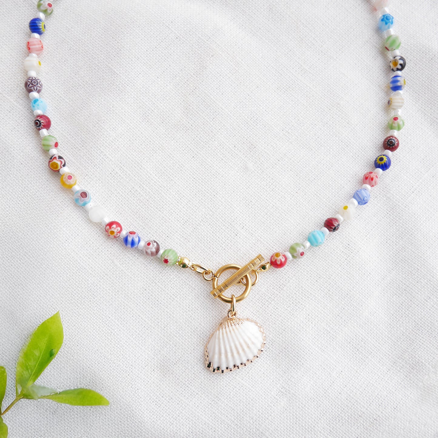 Colorful millefiori necklace with a seashell charm on a white cloth