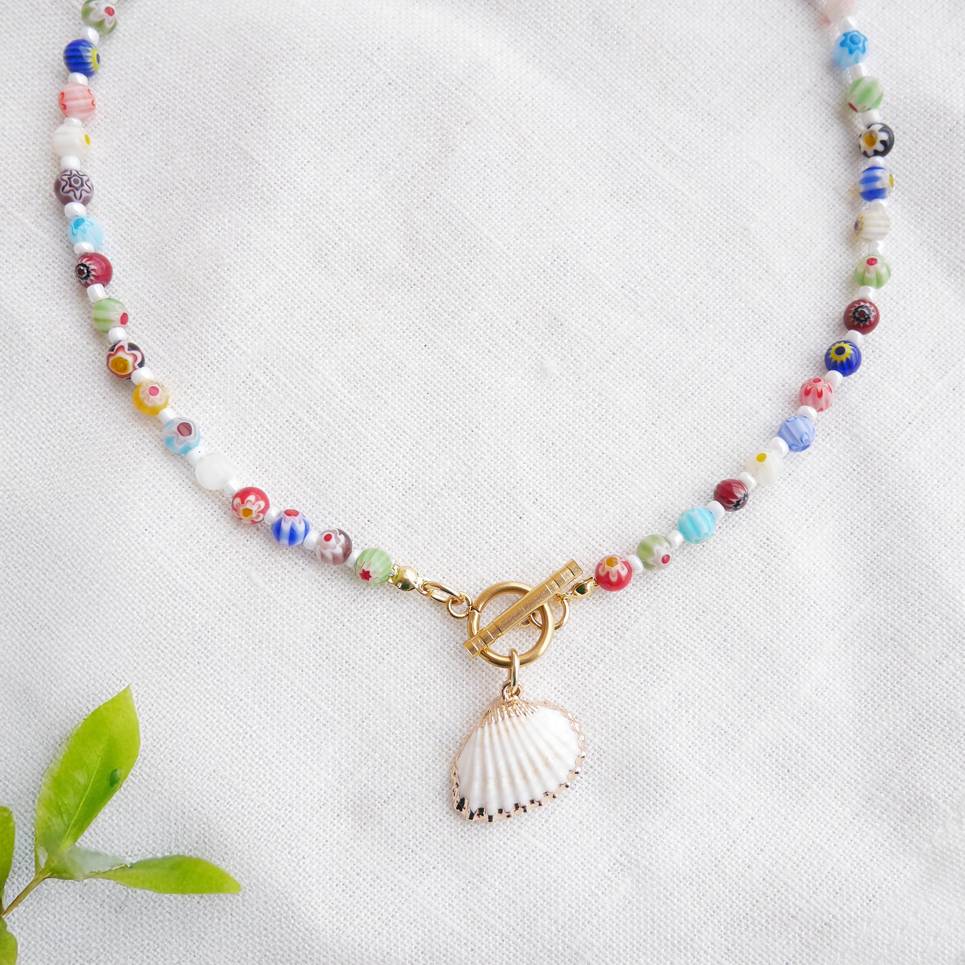 Colorful millefiori necklace with a seashell charm on a white cloth