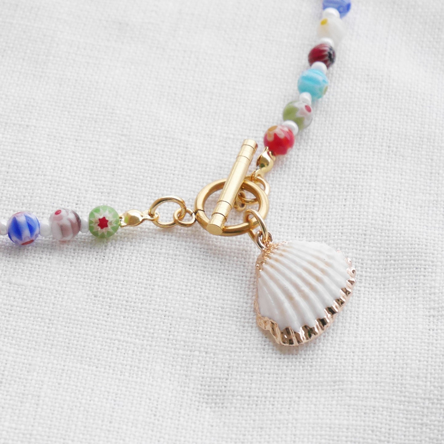 Colorful millefiori necklace with a seashell charm on a white cloth