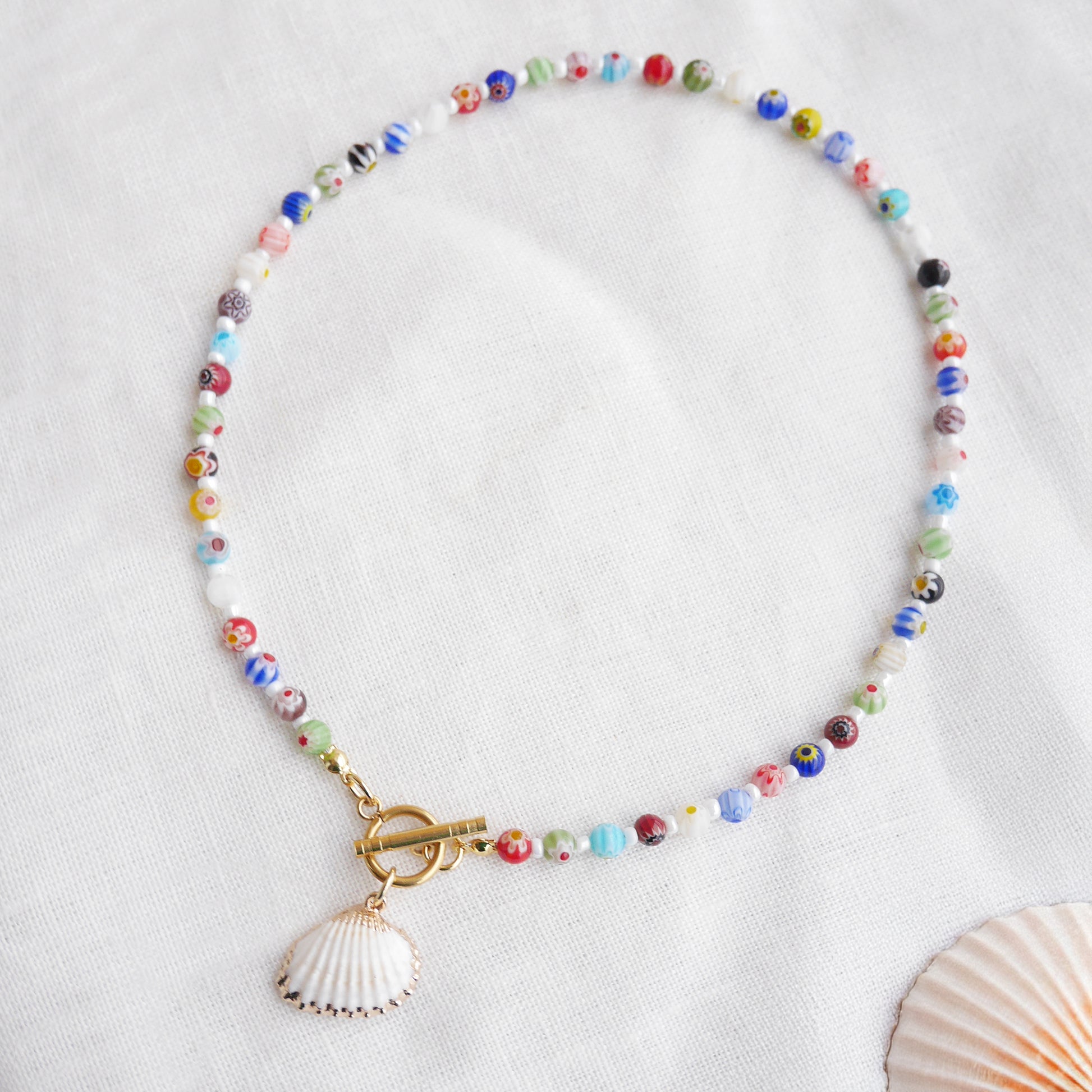 Colorful millefiori necklace with a seashell charm on a white cloth