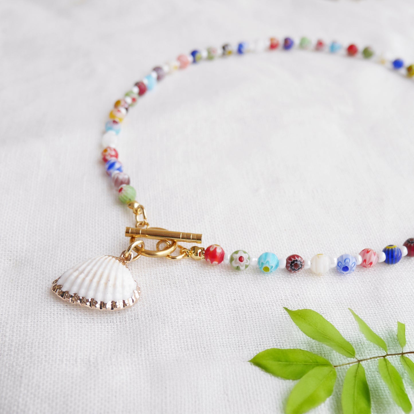 Colorful millefiori necklace with a seashell charm on a white cloth