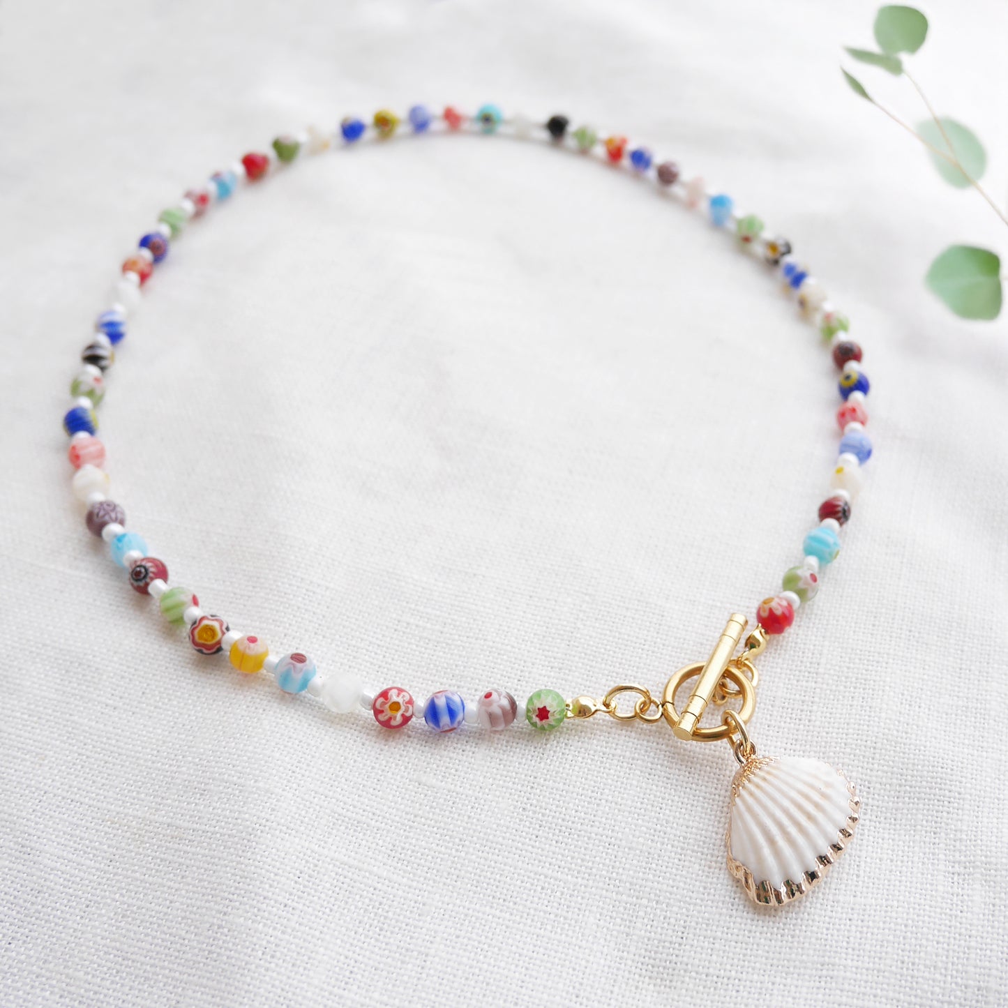 Colorful millefiori necklace with a seashell charm on a white cloth