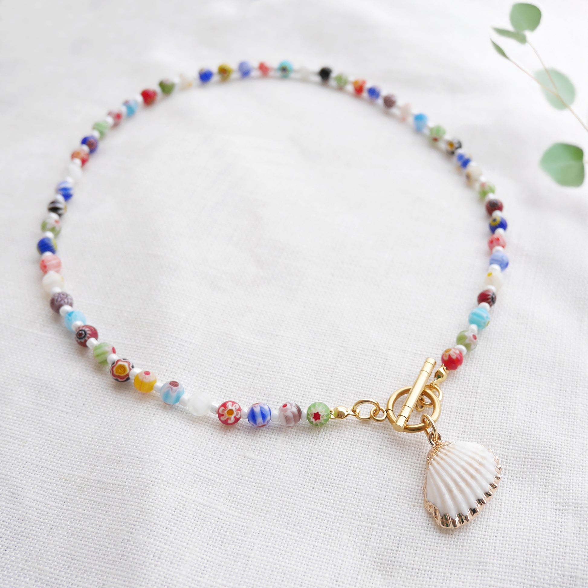 Colorful millefiori necklace with a seashell charm on a white cloth