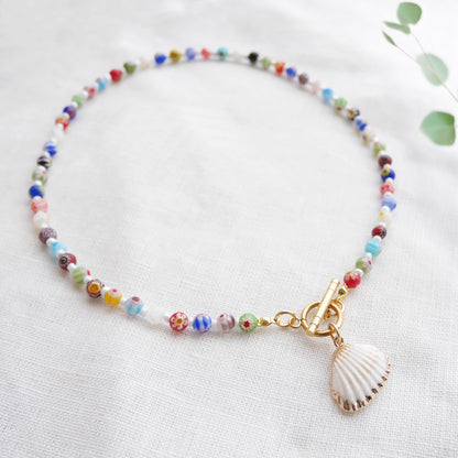 Colorful millefiori necklace with a seashell charm on a white cloth