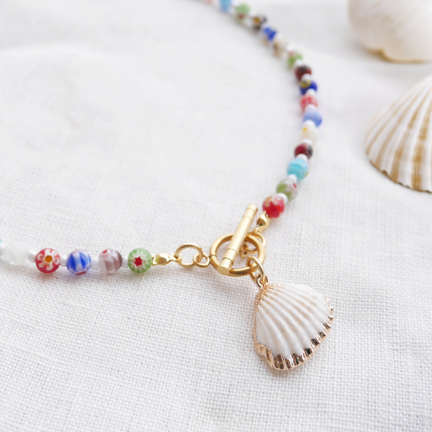 Colorful millefiori necklace with a seashell charm on a white cloth