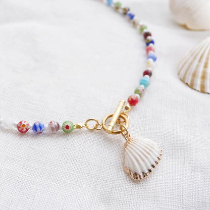 Colorful millefiori necklace with a seashell charm on a white cloth