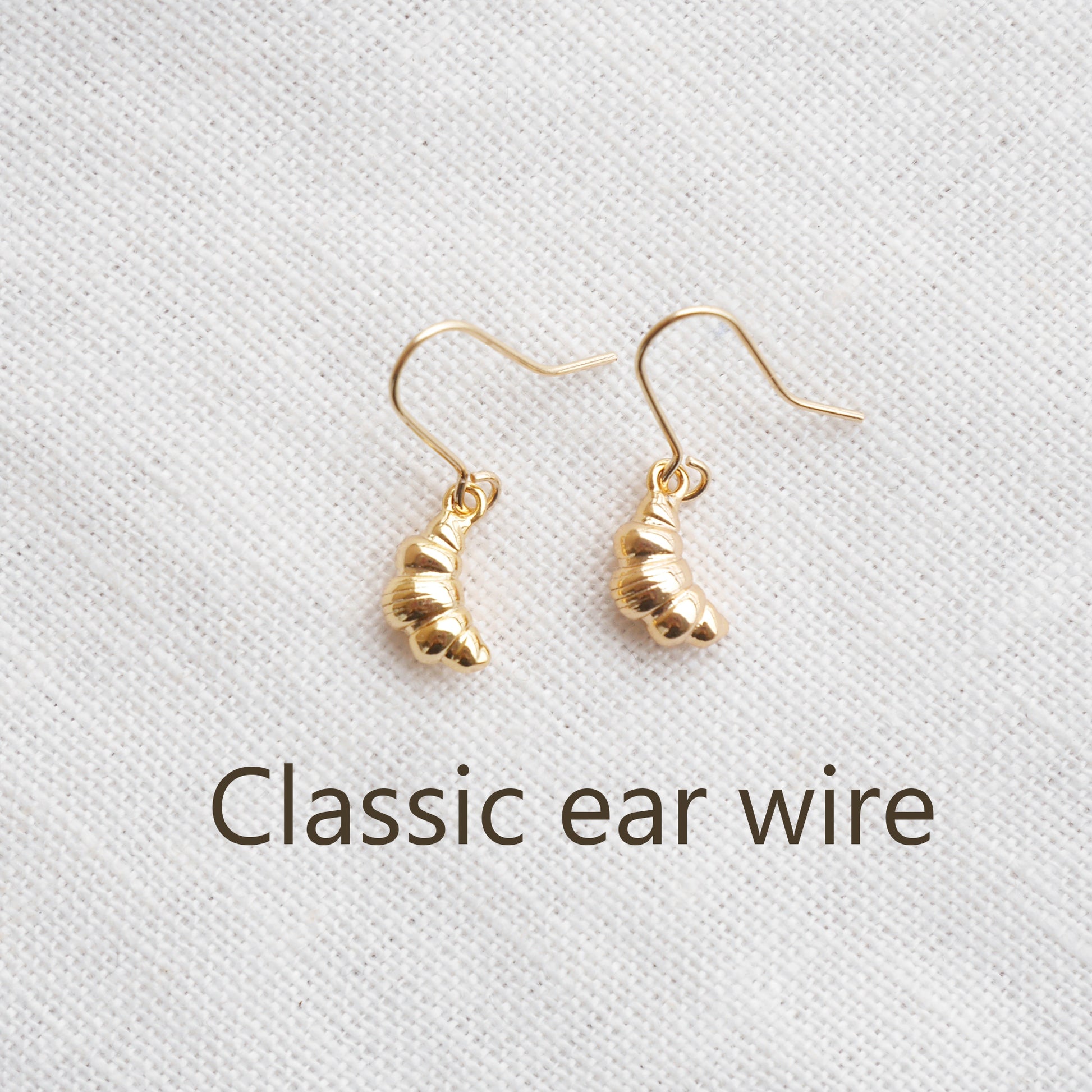 Gold croissant earrings on a textured white surface.