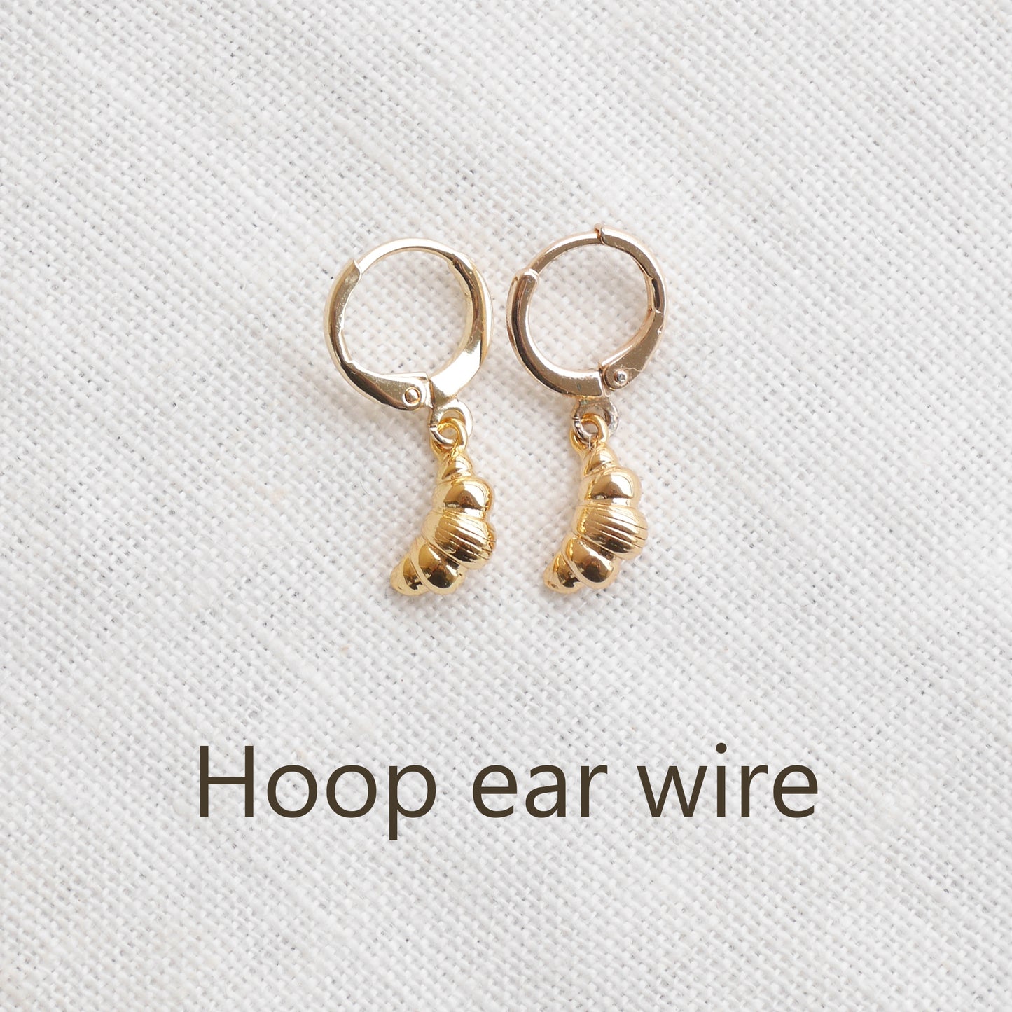 Gold croissant earrings on a textured white surface.