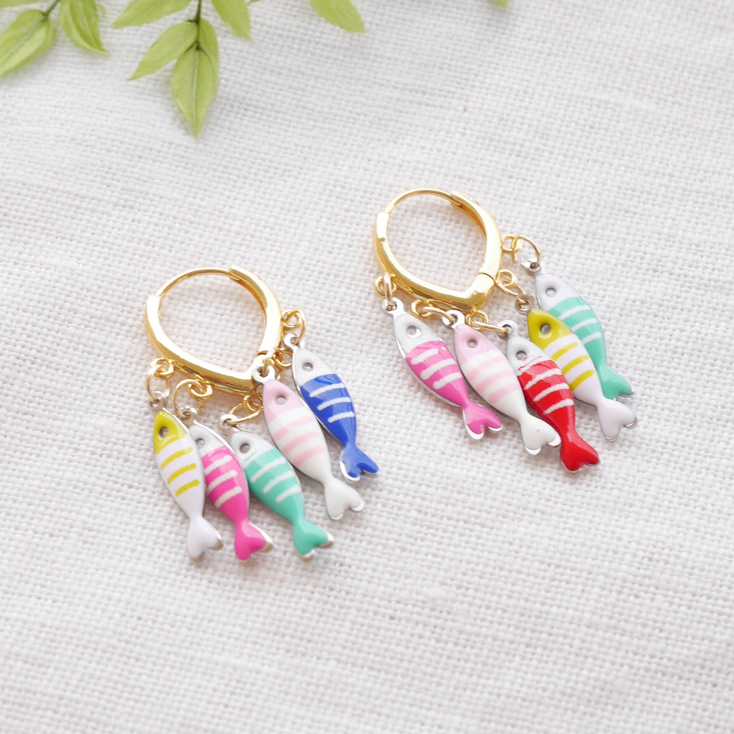 Fish charm hoop earrings on a white cloth.