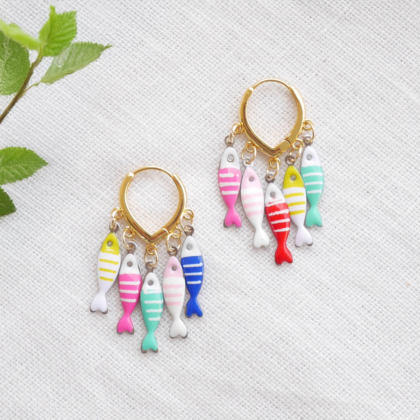 Fish charm hoop earrings on a white cloth.