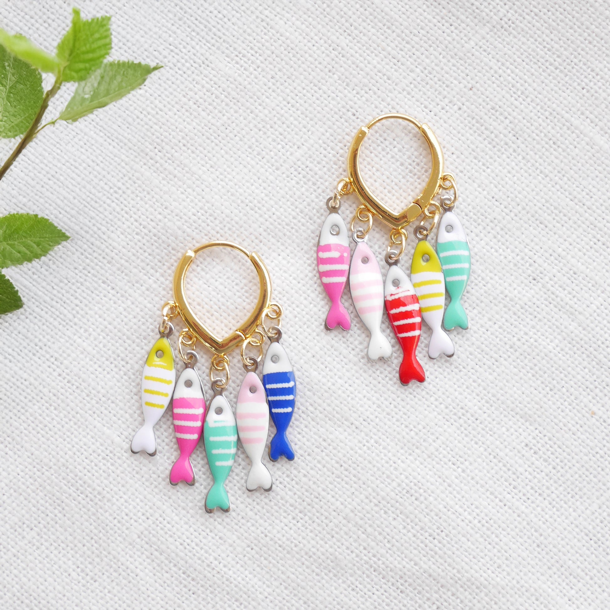 Fish charm hoop earrings on a white cloth.