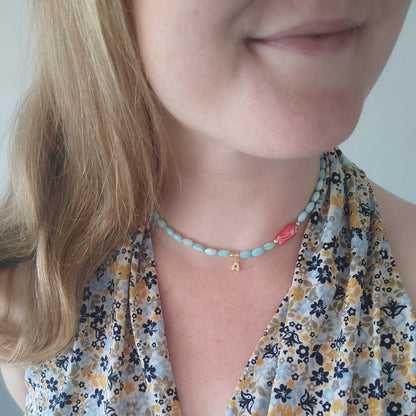 Woman wearing turquoise beaded necklace with red fish and gold bubble initial charm.