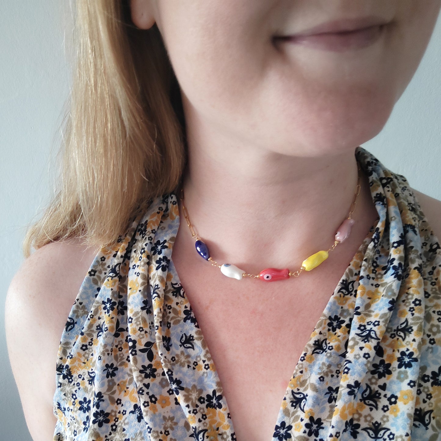 Woman wearing a paperclip chain necklace with five colorful porcelain fish beads.