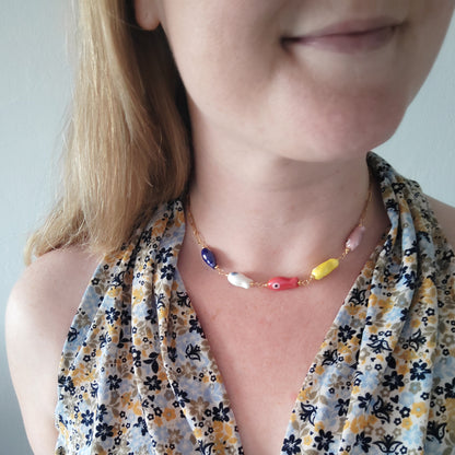 Woman wearing a paperclip chain necklace with five colorful porcelain fish beads.
