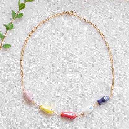 Paperclip chain necklace with five colorful porcelain fish beads, on a white cloth.
