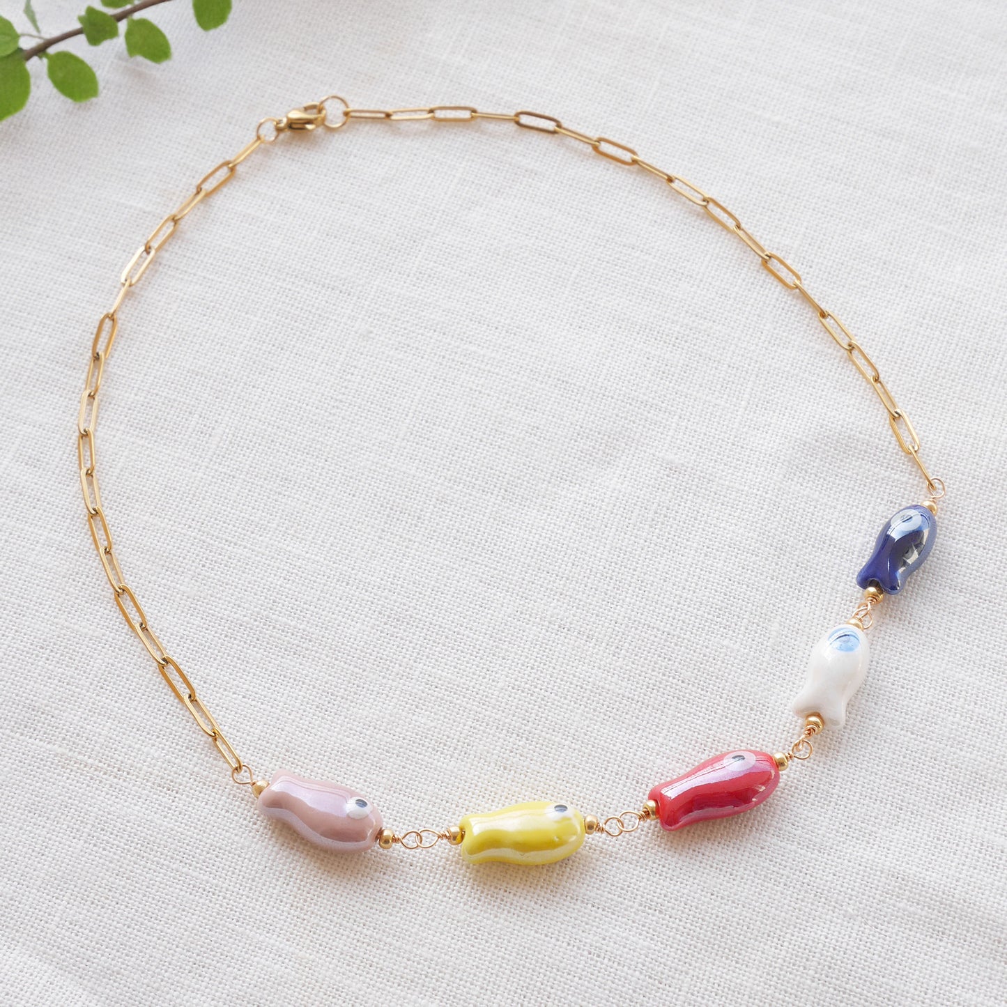 Paperclip chain necklace with five colorful porcelain fish beads, on a white cloth.
