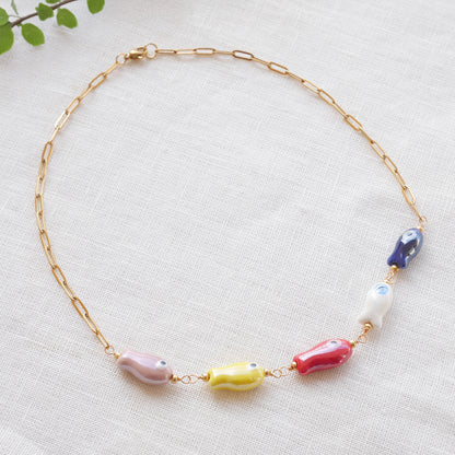 Paperclip chain necklace with five colorful porcelain fish beads, on a white cloth.