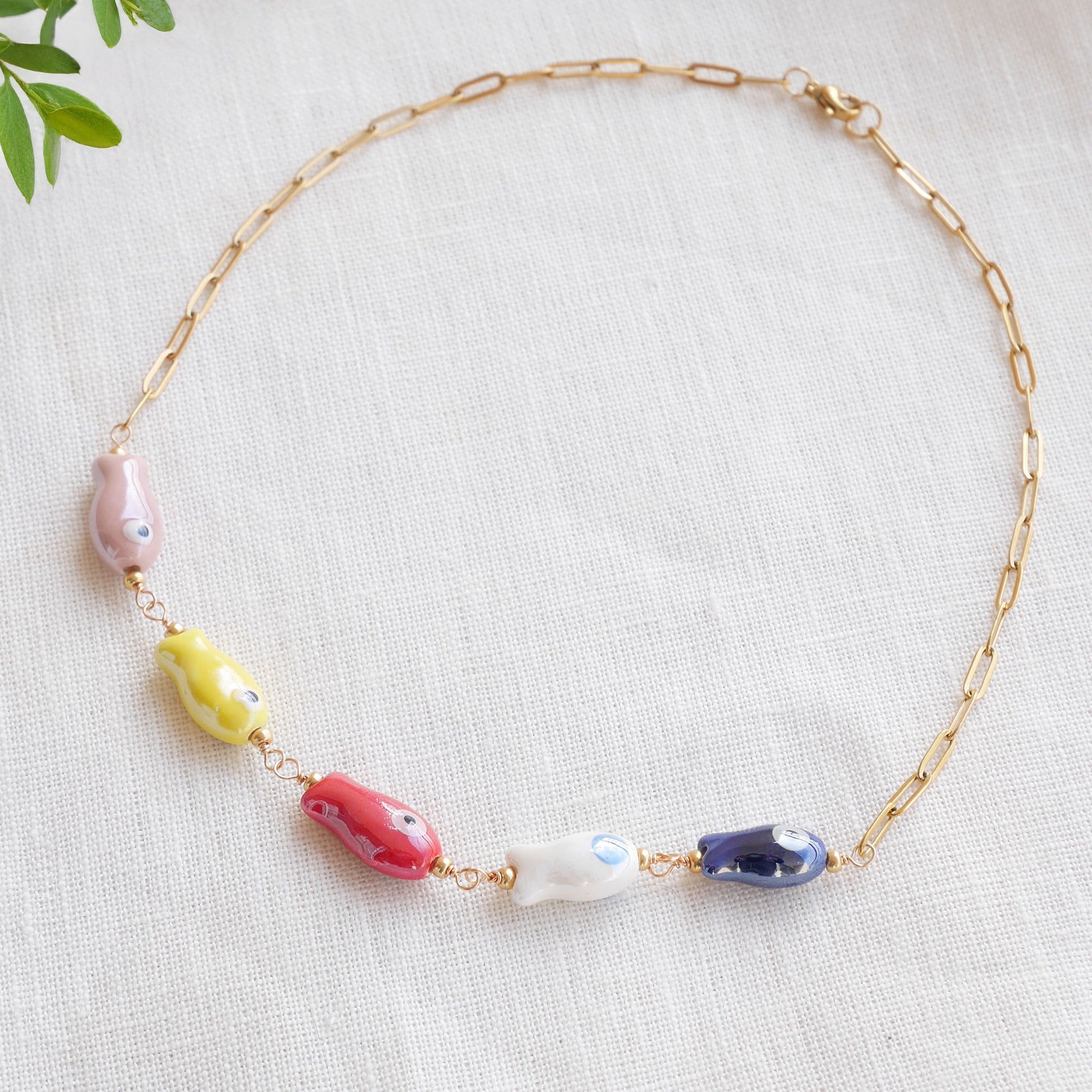 Paperclip chain necklace with five colorful porcelain fish beads, on a white cloth.