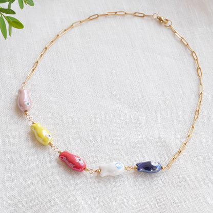 Paperclip chain necklace with five colorful porcelain fish beads, on a white cloth.