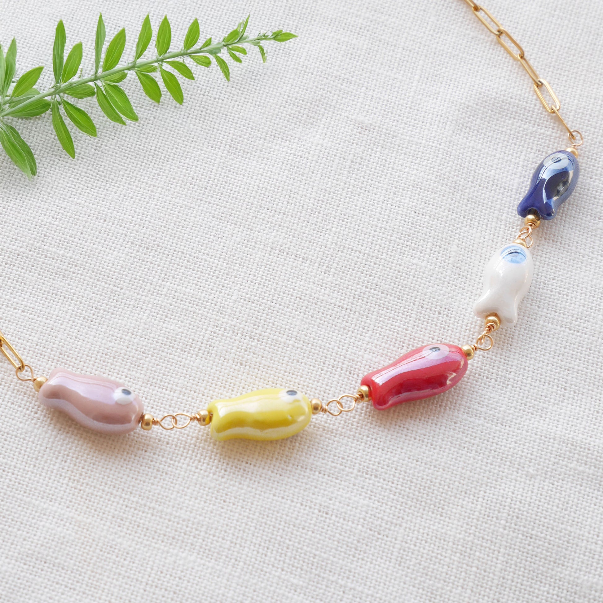 Paperclip chain necklace with five colorful porcelain fish beads, on a white cloth.