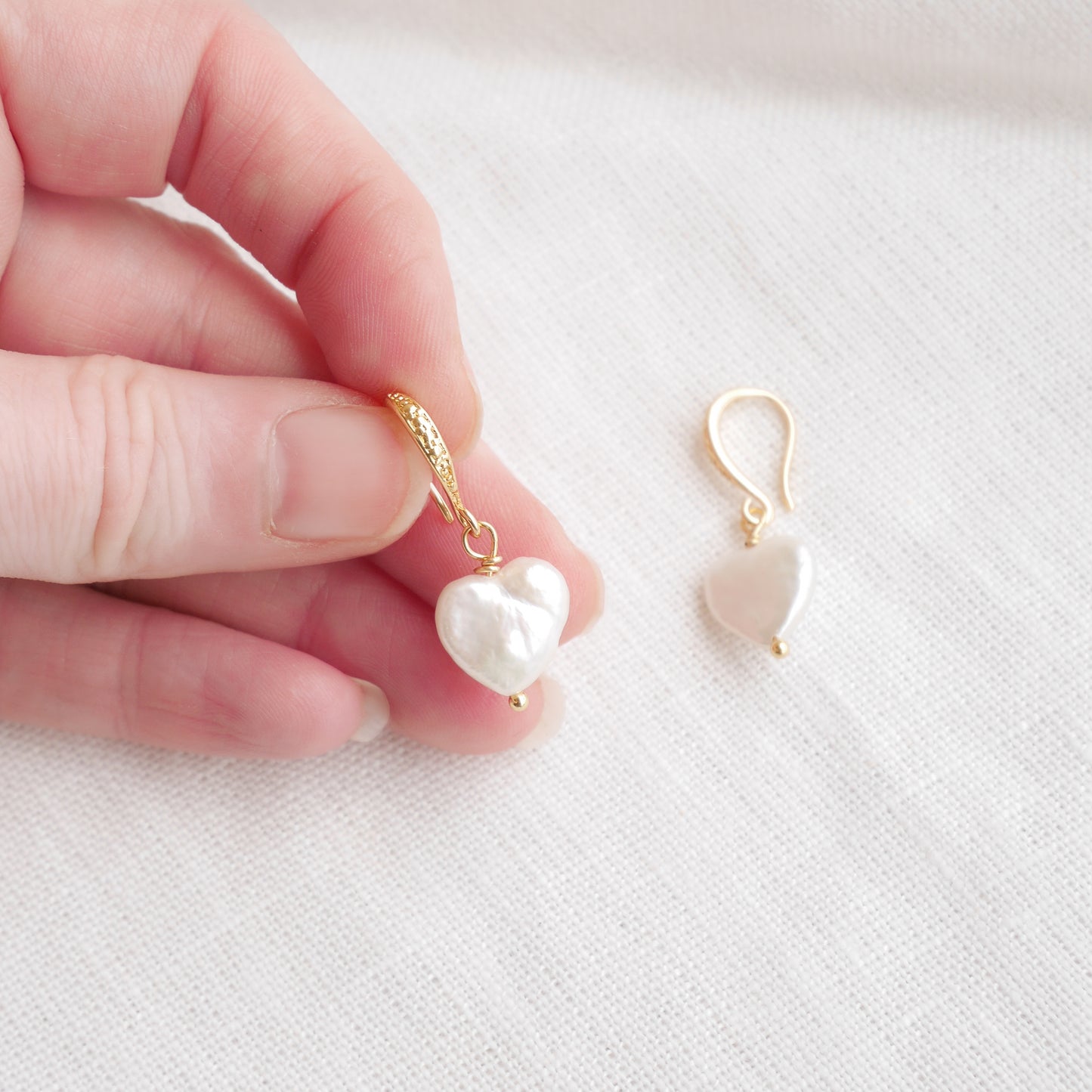 Freshwater pearl heart earrings on a white cloth.