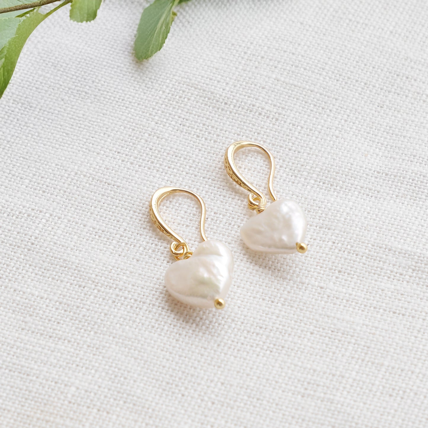 Freshwater pearl heart earrings on a white cloth.