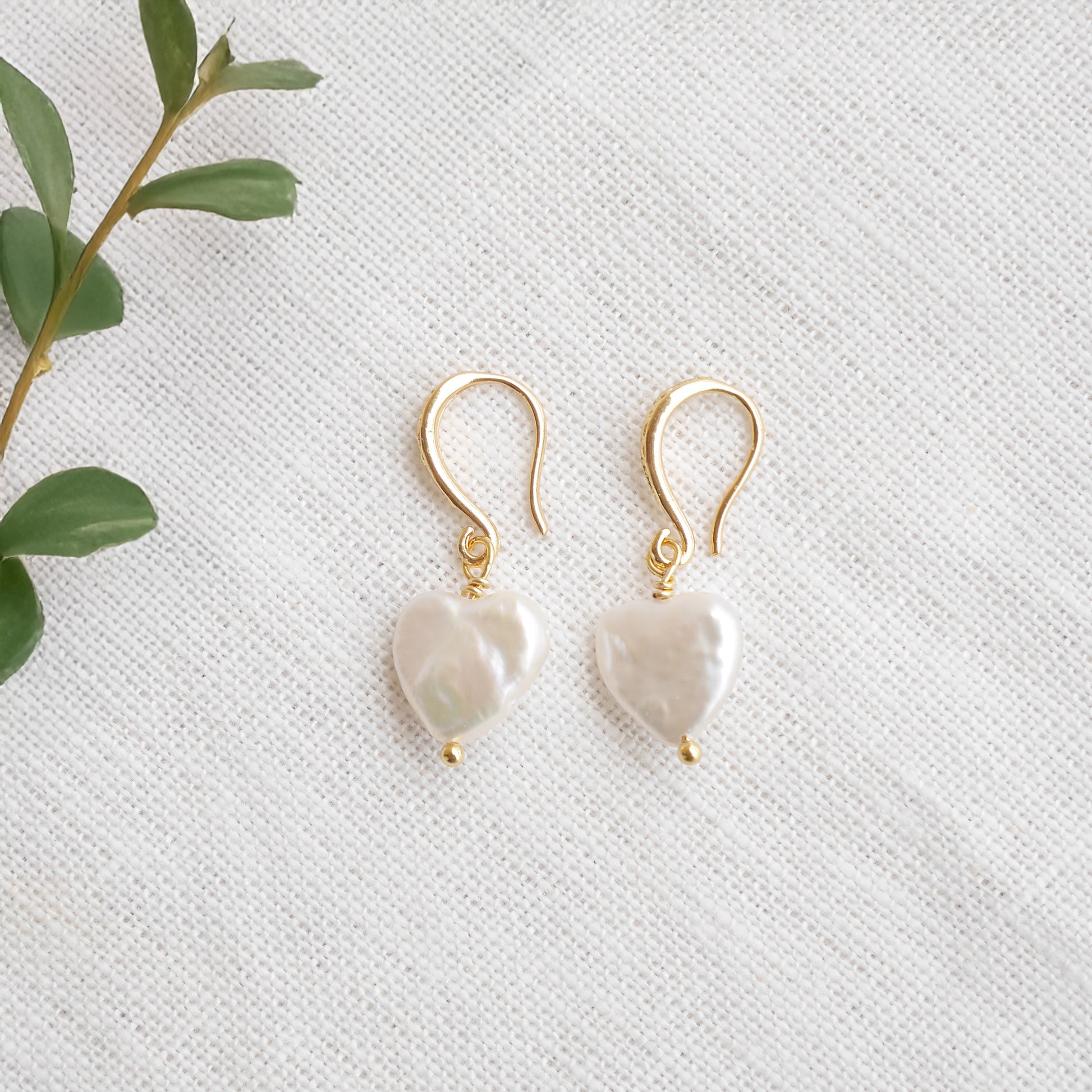 Freshwater pearl heart earrings on a white cloth.