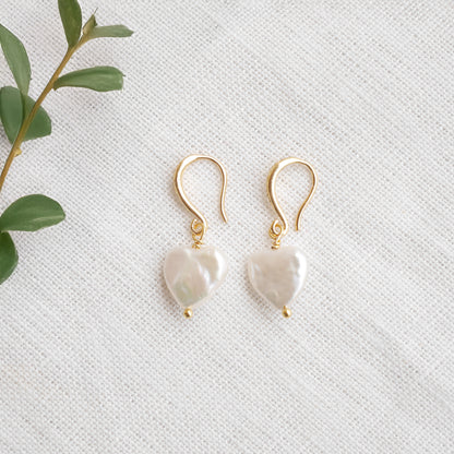 Freshwater pearl heart earrings on a white cloth.
