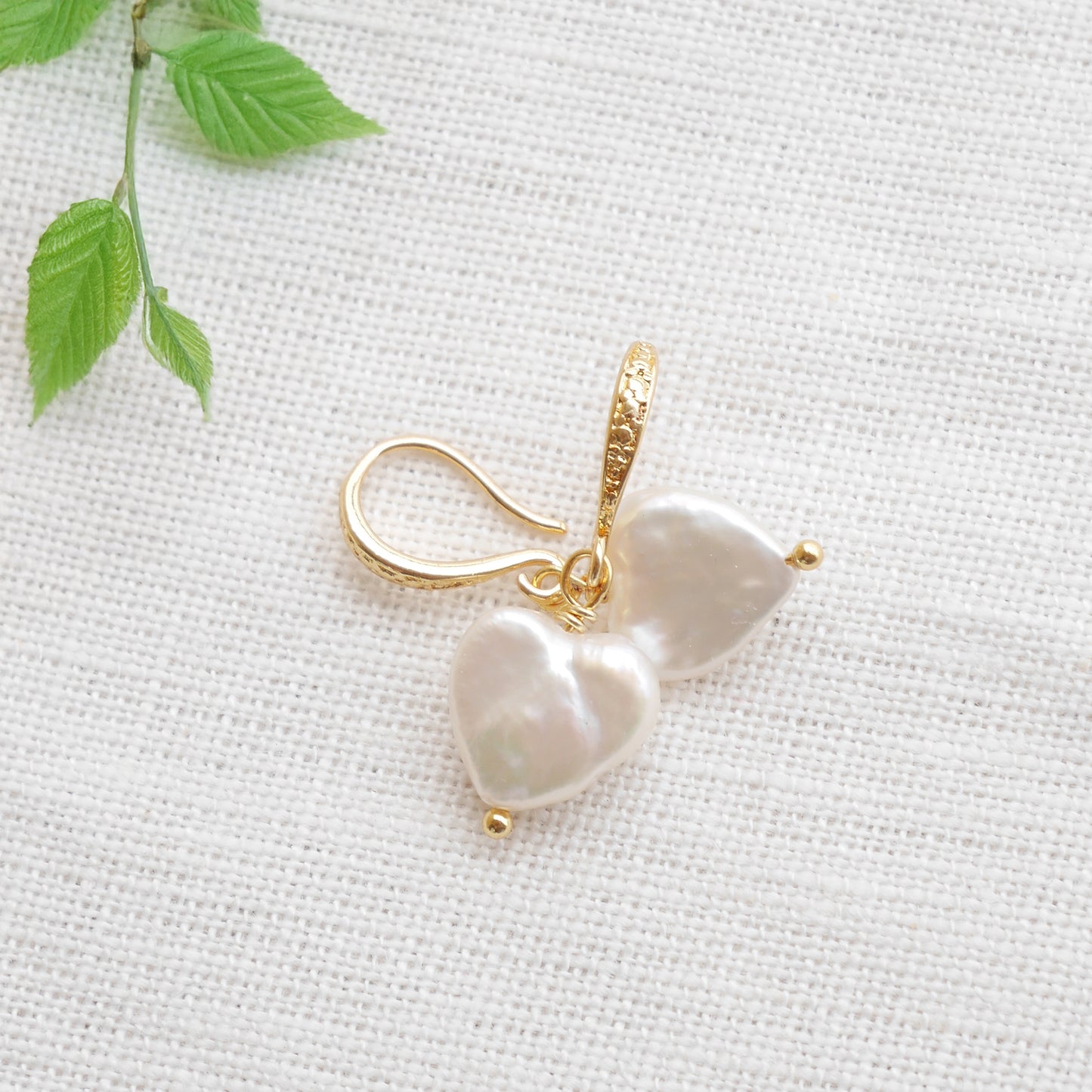 Freshwater pearl heart earrings on a white cloth.