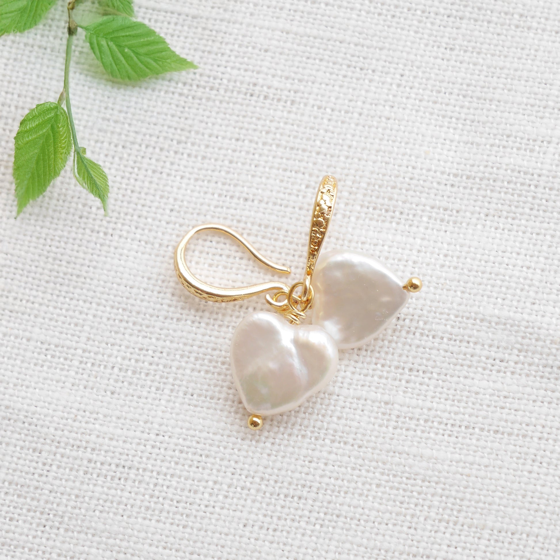 Freshwater pearl heart earrings on a white cloth.