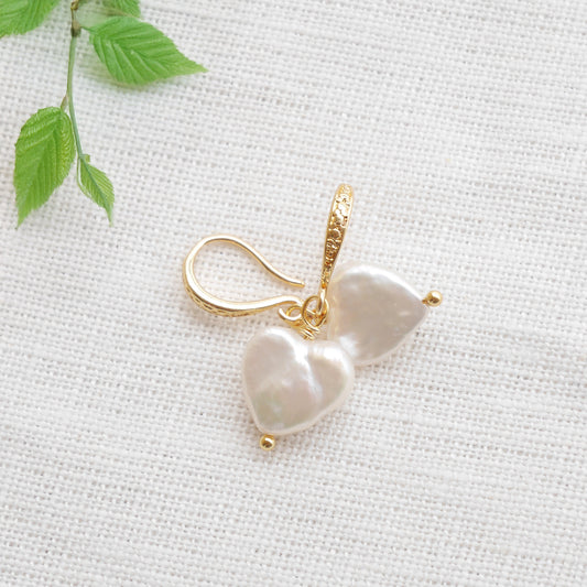 Freshwater pearl heart earrings on a white cloth.