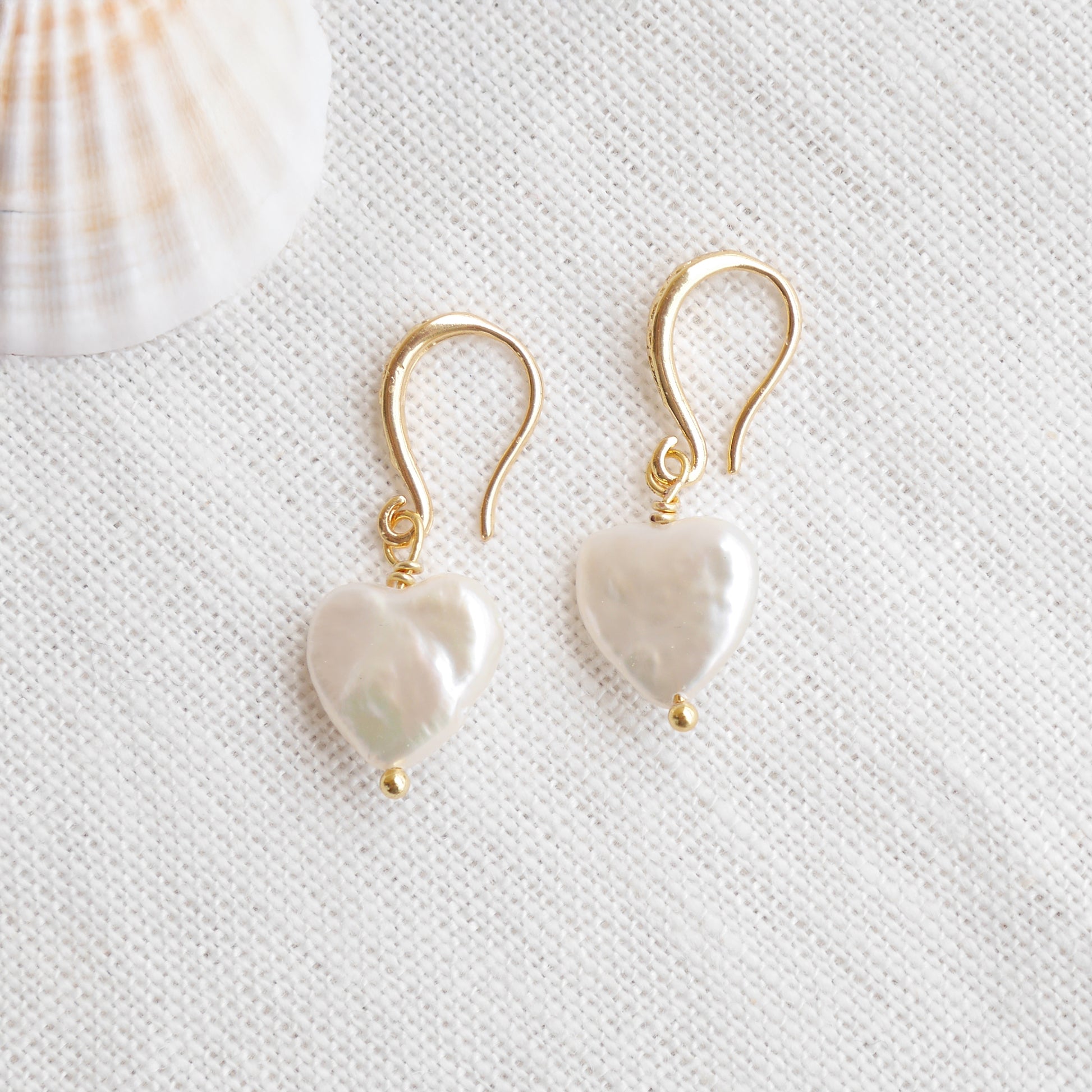 Freshwater pearl heart earrings on a white cloth.