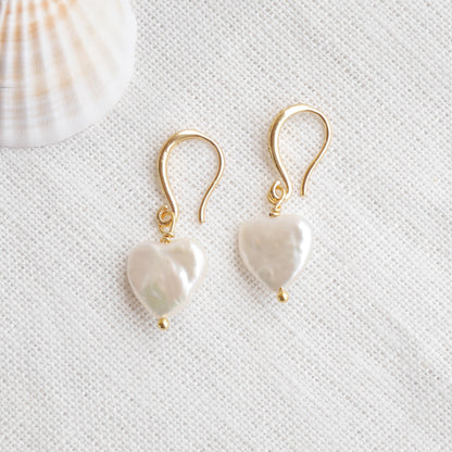 Freshwater pearl heart earrings on a white cloth.