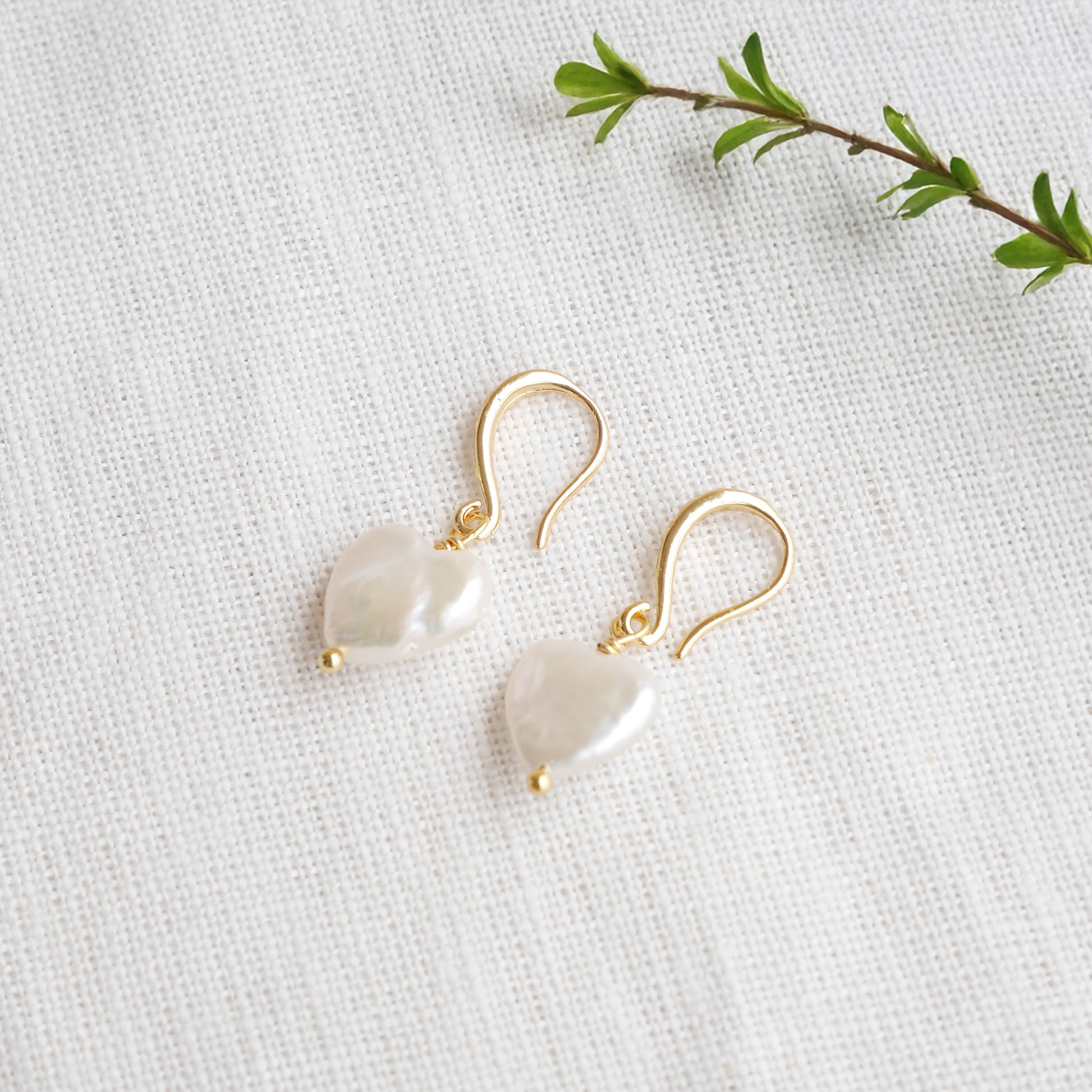 Freshwater pearl heart earrings on a white cloth.