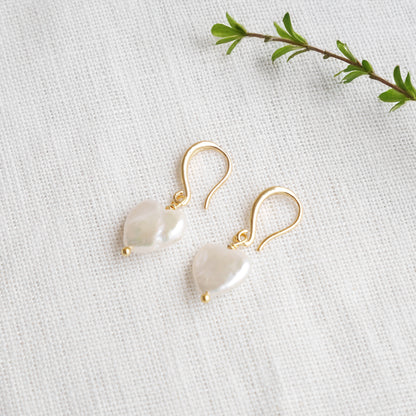 Freshwater pearl heart earrings on a white cloth.