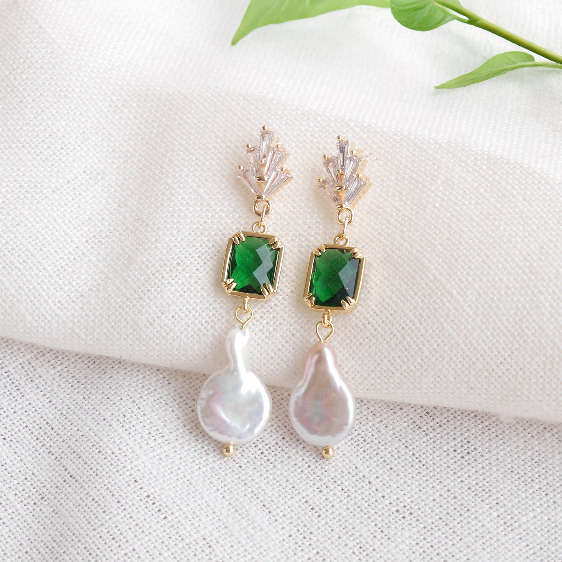Green art deco style dangle earrings on a white cloth.