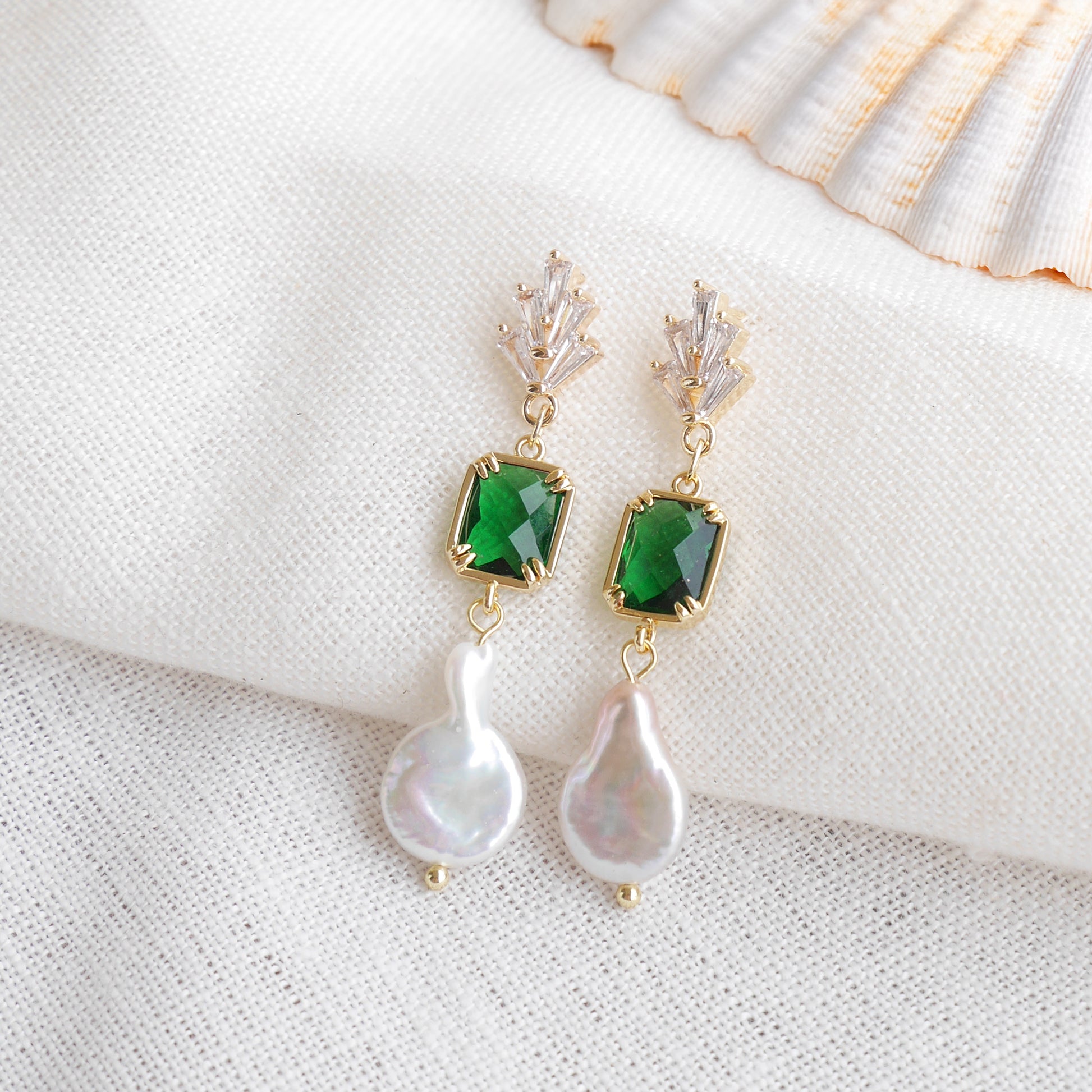 Green art deco style dangle earrings on a white cloth.